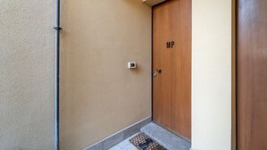 A hallway with a wooden door labeled 'MP,' a wall-mounted light fixture, and a tiled floor.