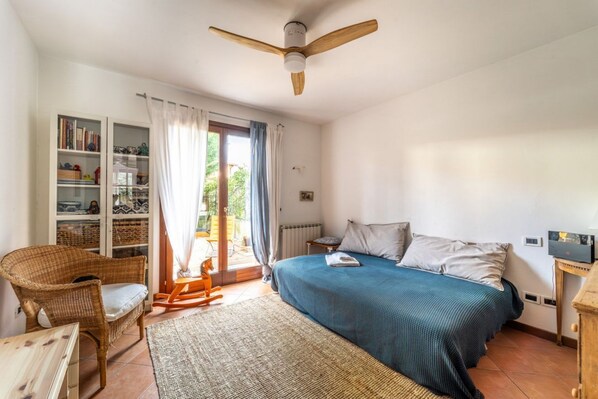 A bedroom with a bed, a chair, a table, a bookshelf, and a ceiling fan.