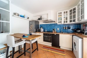 A compact kitchen with white cabinets, a blue tiled backsplash, a microwave, stove, and a washing machine.