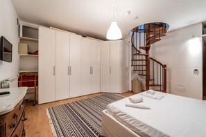 A bedroom with a bed, a wooden spiral staircase, a white wardrobe, and a small desk with a chair.