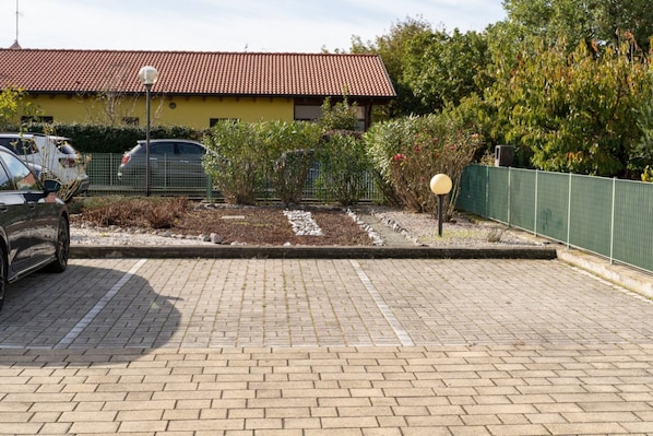A paved parking area with a yellow building and a red-tiled roof in the background.