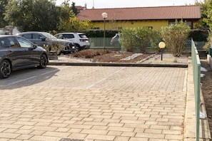 A parking area with a paved surface, a yellow building with a red roof, and a green fence.