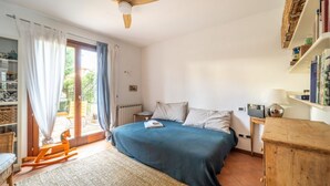 A bedroom with a bed, a wooden rocking chair, a bookshelf, and a ceiling fan.