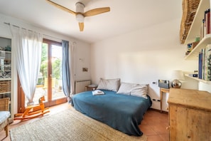A bedroom with a bed, a wooden rocking chair, a bookshelf, and a ceiling fan.