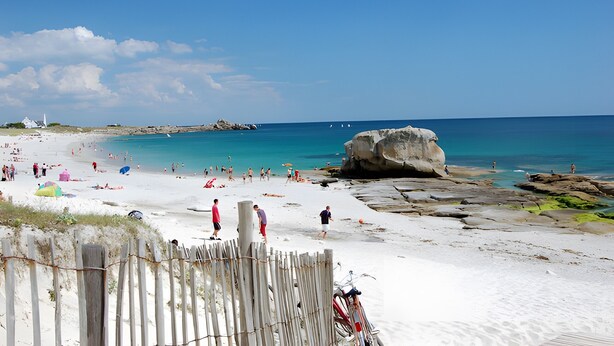 Une plage avec des gens, une grande formation rocheuse et une clôture en bois.