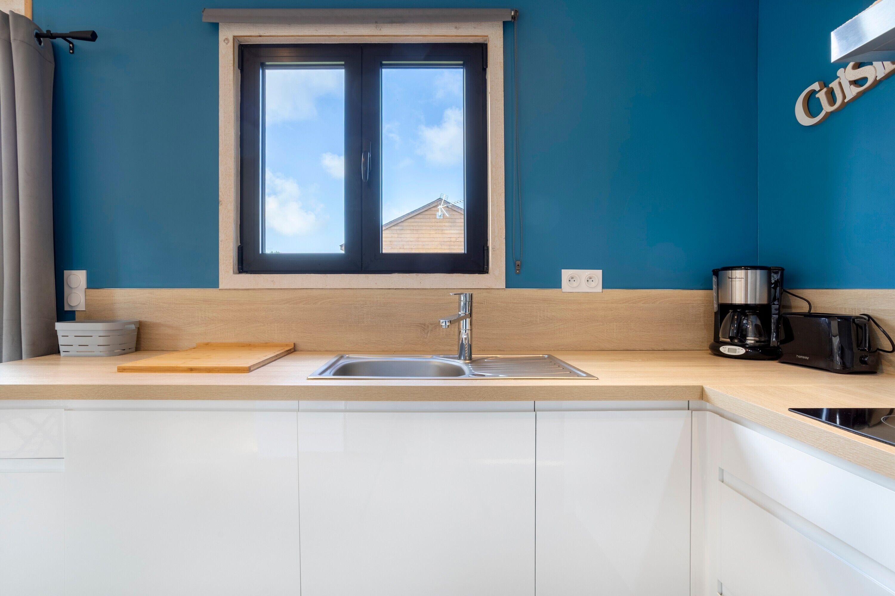 A kitchen with a window, a sink, a cutting board, and a coffee maker.