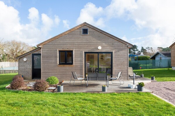 Ein modernes Haus mit Holzfassade, einer großen Schiebetür aus Glas und einer Terrasse mit Gartenmöbeln.