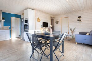 Eine moderne Küche mit weißen Schränken, ein Essbereich mit Tisch und Stühlen und ein blaues Sofa in einem hellen Raum mit Holzboden und weißer Decke.
