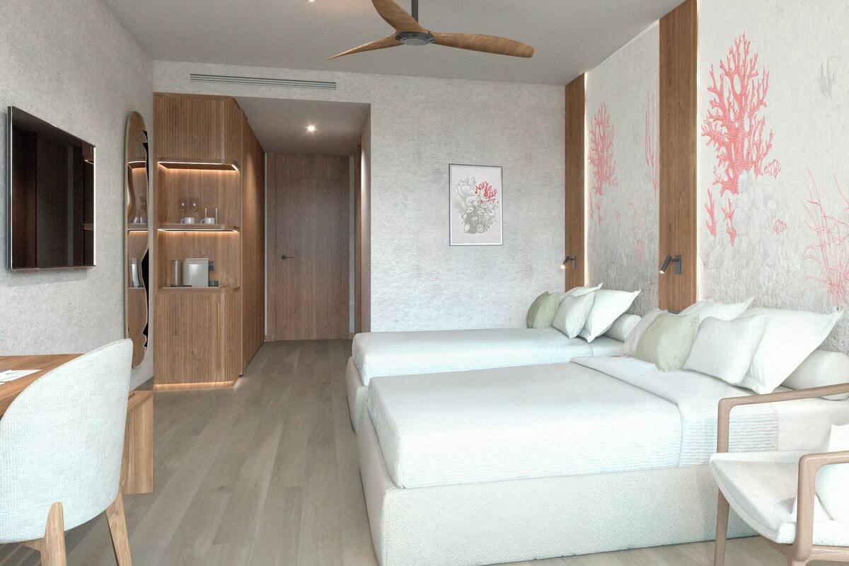 Una habitació d'hotel moderna amb un llit, dues taules de nit, un escriptori, una cadira, un ventilador de sostre i una televisió penjada a la paret.