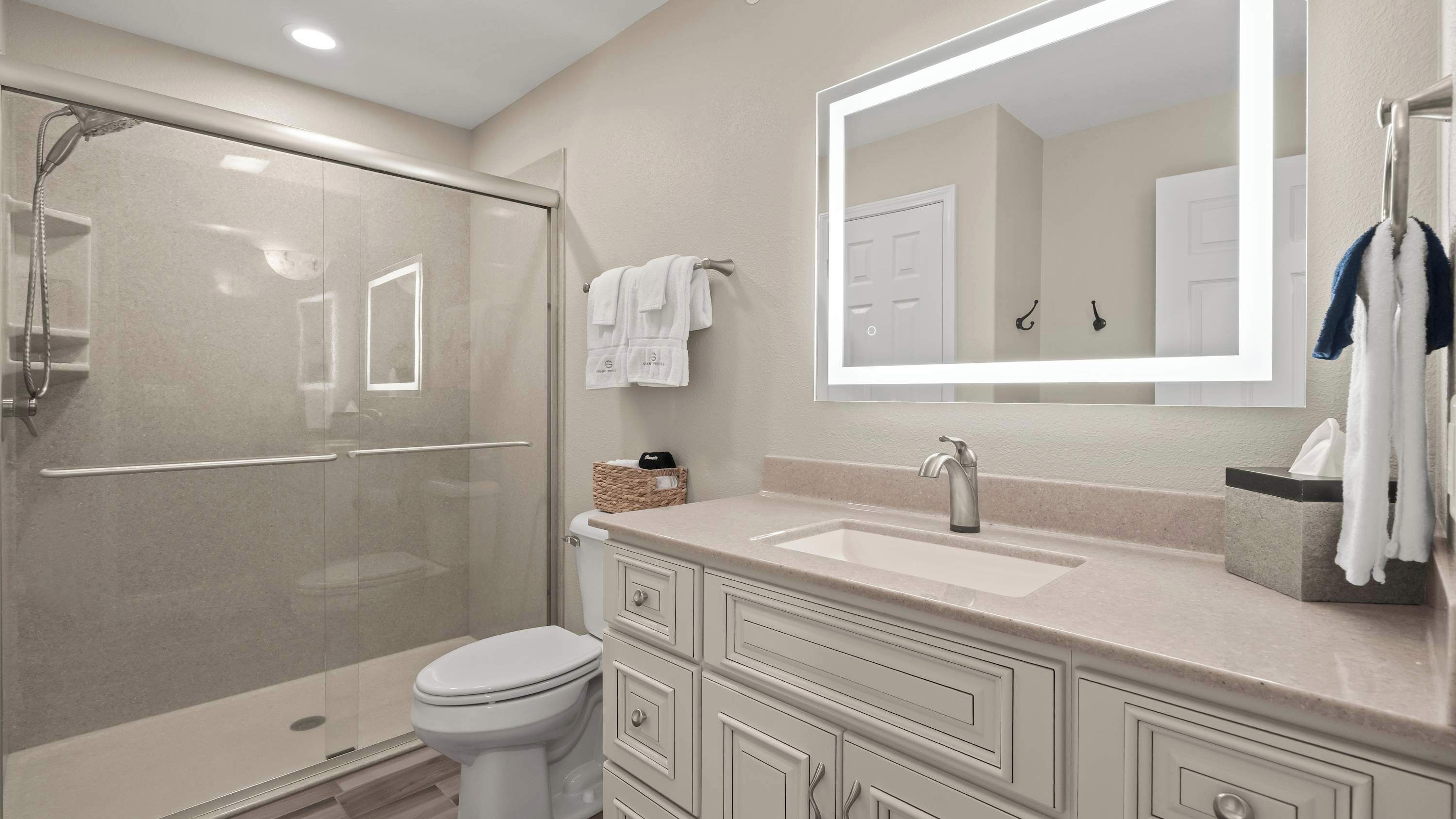 Une salle de bain moderne avec une douche à parois de verre, des toilettes blanches, un meuble-lavabo avec un miroir et un porte-serviettes avec des serviettes.