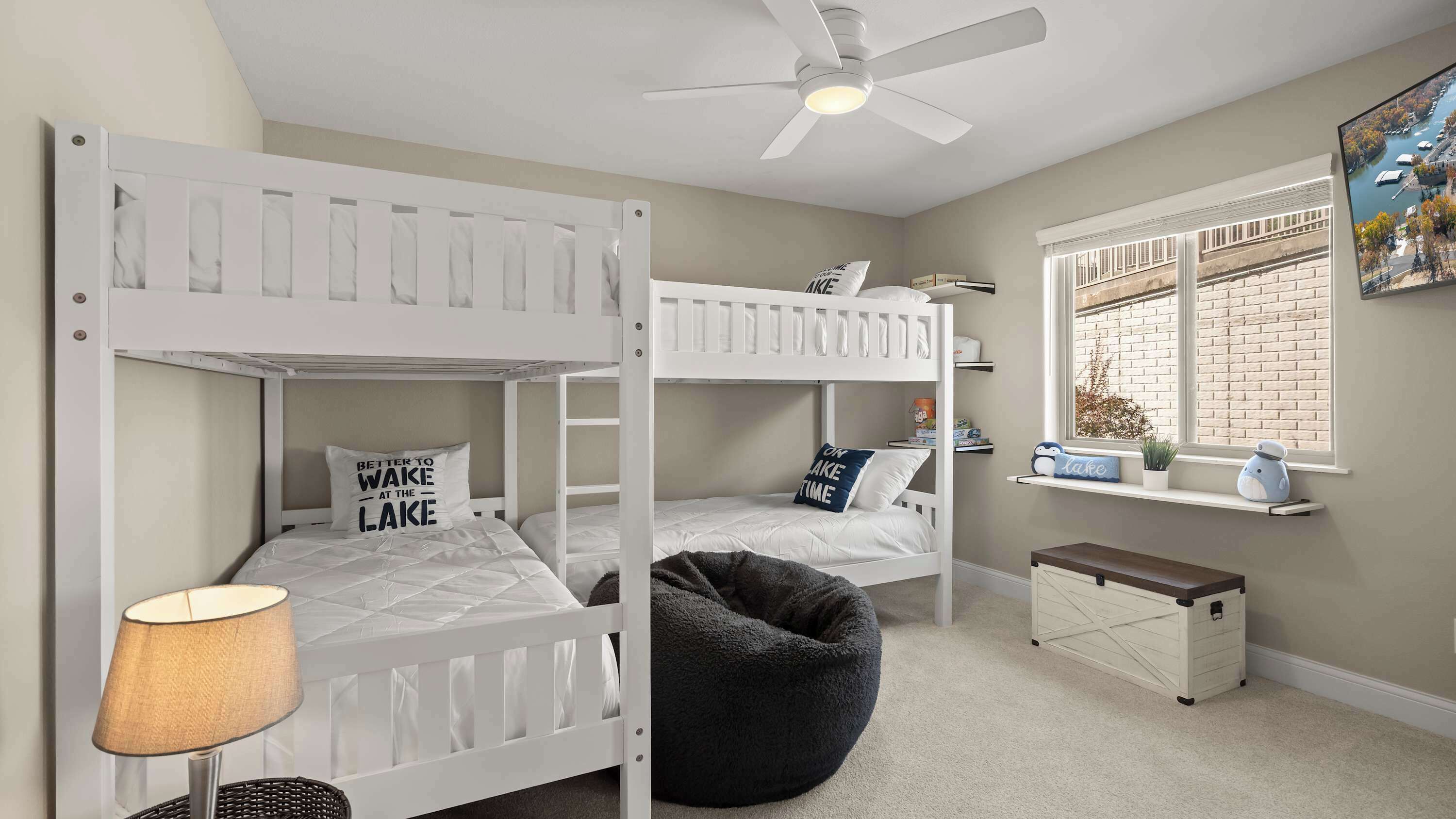 A bunk bed room with a ceiling fan, a window with a view of a lake, and a small shelf with decorative items.