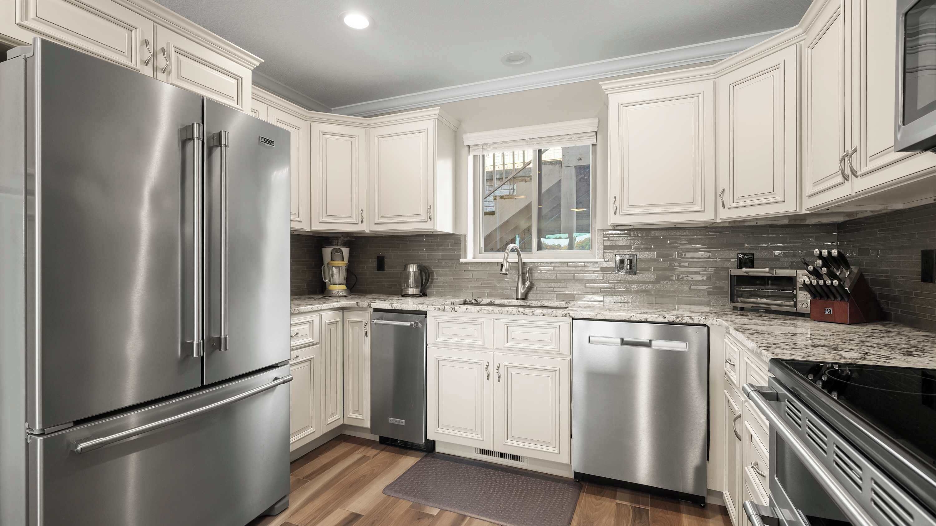 A modern kitchen with stainless steel appliances, white cabinetry, a granite countertop, and a backsplash of gray tiles.