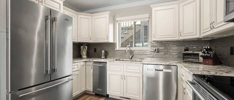 A modern kitchen with stainless steel appliances, white cabinetry, a granite countertop, and a backsplash of gray tiles.