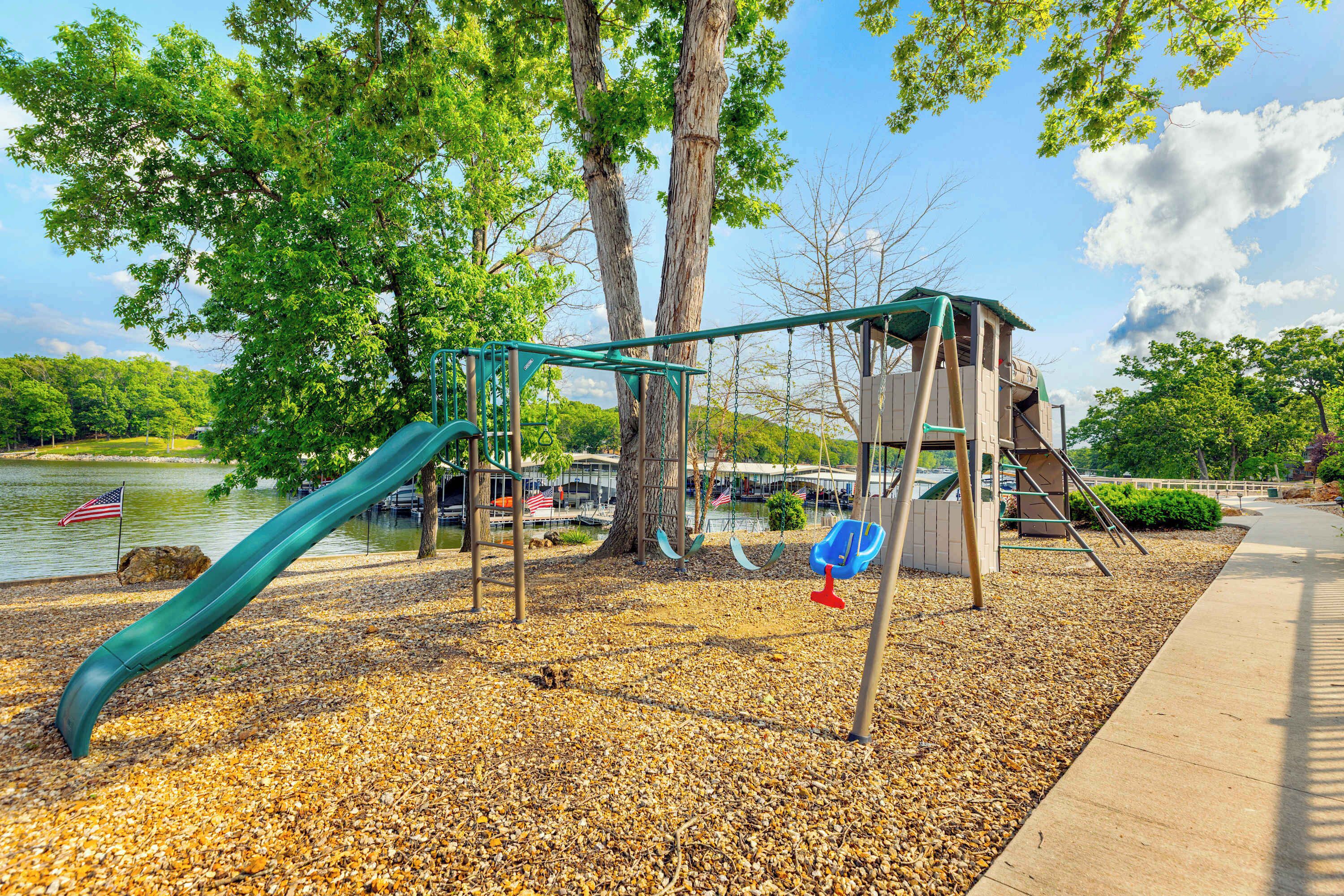 Un parque infantil con tobogán, columpios y una estructura para escalar, cerca de un lago.