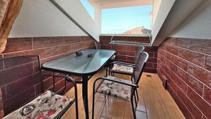 En lille lukket balkon med et bord, stole, grill og udsigt til himlen.