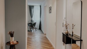 Ein moderner Flur mit Holzboden, einem runden Tisch mit einer Vase und einem Schild, sowie einem Spiegel an der Wand.