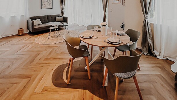 Ein modernes Wohnzimmer mit Essbereich, ausgestattet mit einer Couch, einem runden Esstisch mit Stühlen und großen Fenstern mit Vorhängen.