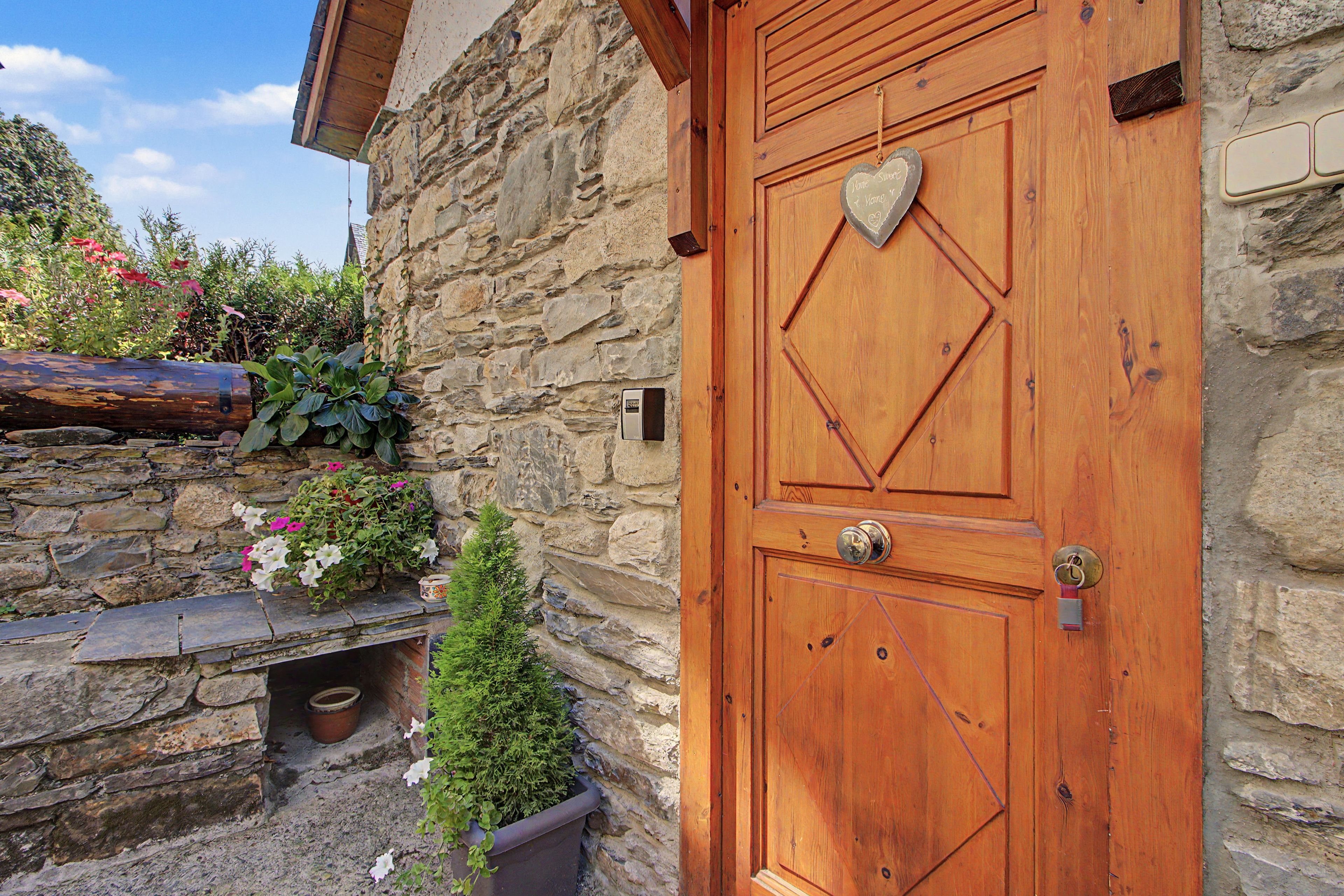 A wooden door with a heart-shaped decoration, a stone wall, and a small potted plant.