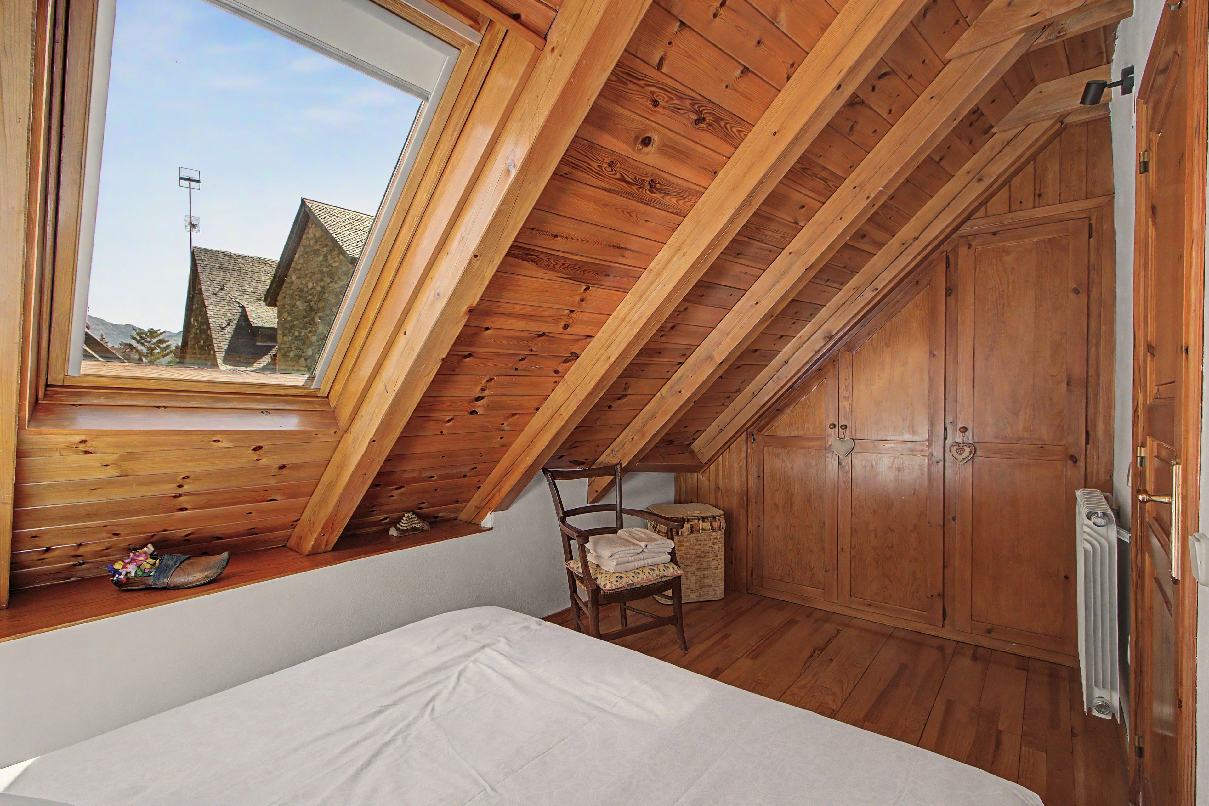 Ein Zimmer mit schrägen Wänden, Holztäfelung, einem Bett, einem Sessel und einer Heizung.