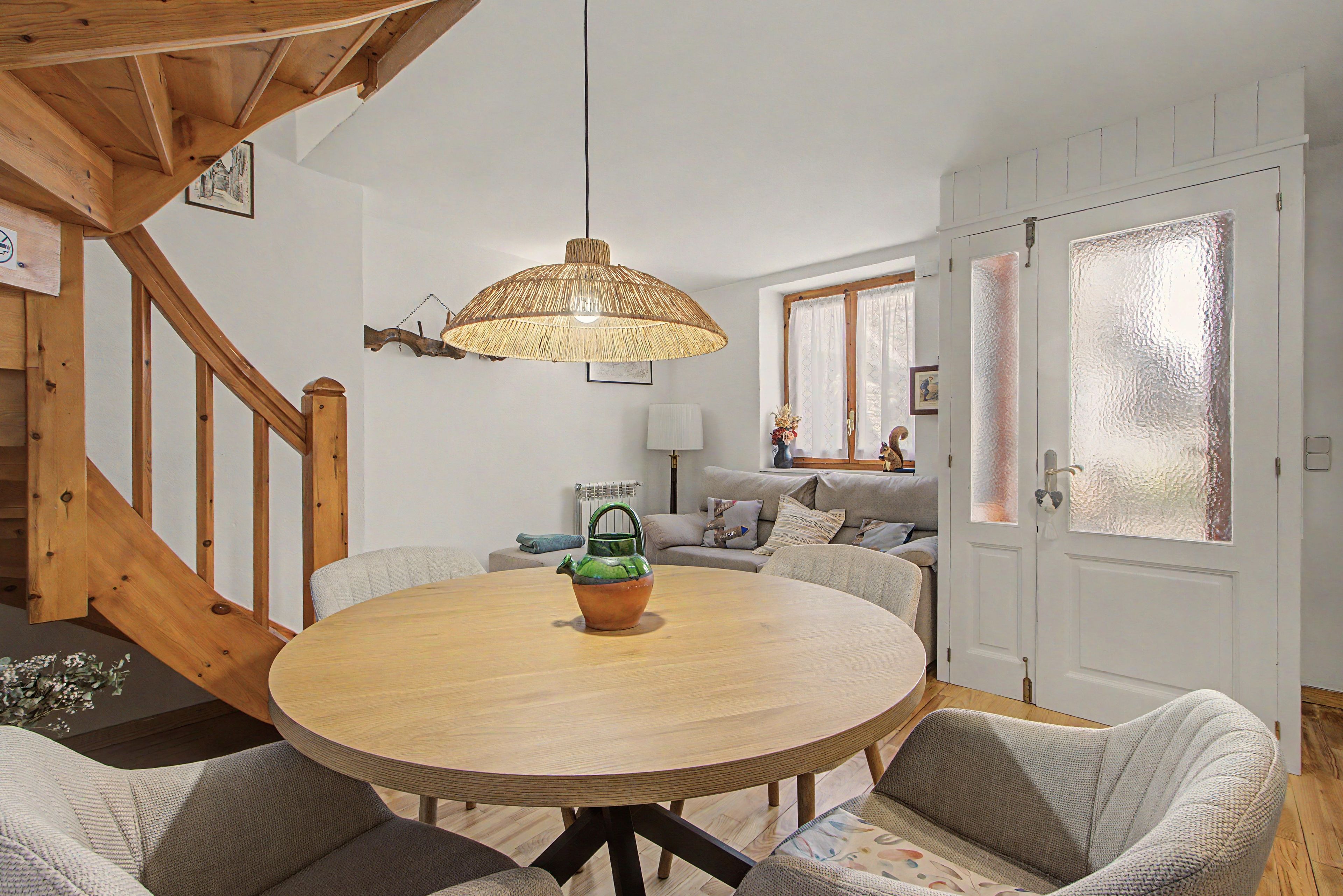 Un salon chaleureux avec une table ronde en bois, une bouilloire verte et un luminaire suspendu en fibres tressées.