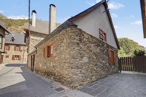 A stone building with a sloped roof, wooden shutters, and a paved street.