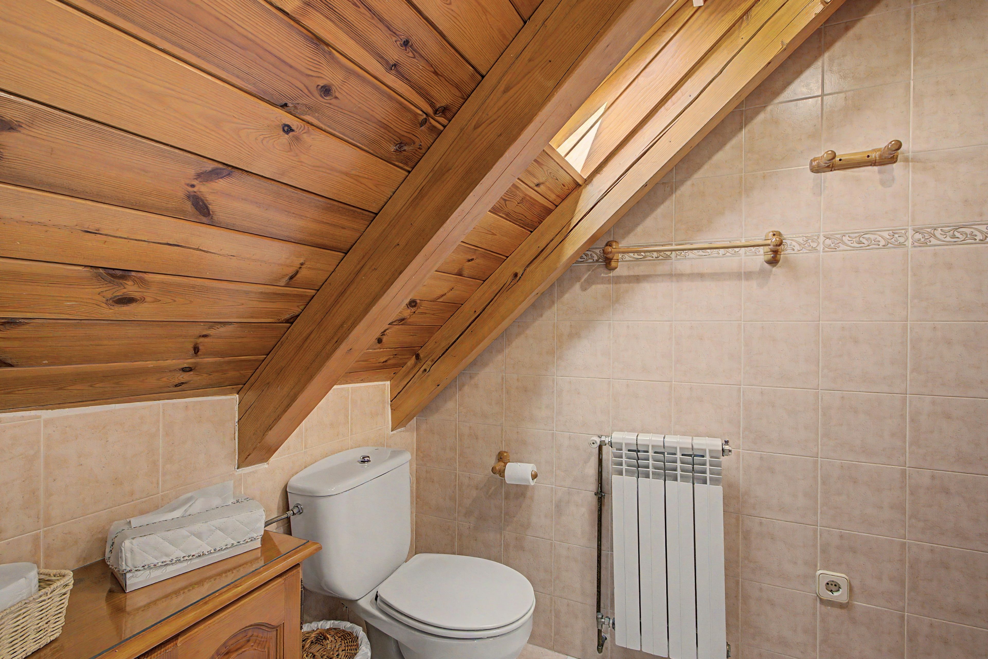 A bathroom with a wooden ceiling, a toilet, a towel rack, and a radiator.