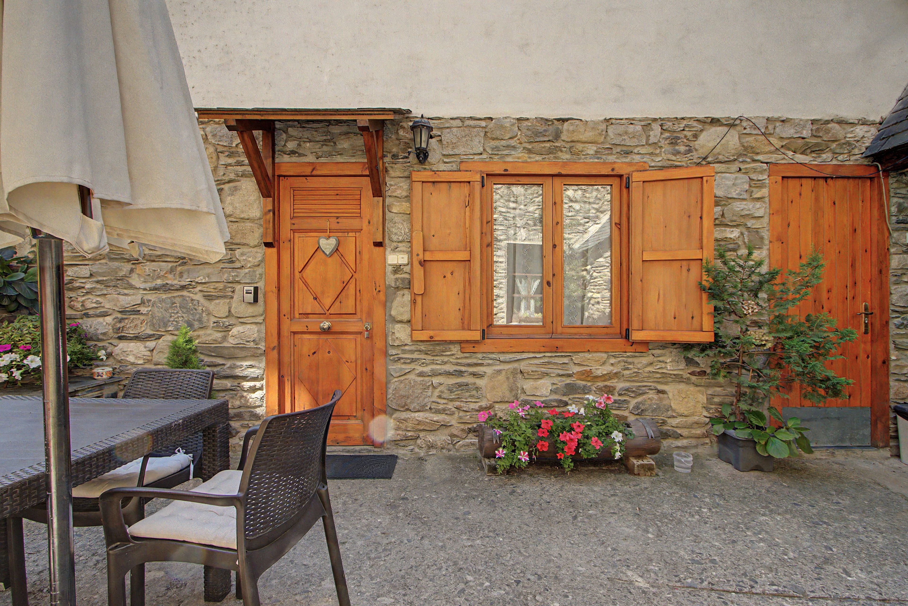 Un bâtiment en pierre avec des portes et des fenêtres en bois, une table avec des chaises et des plantes en pot.