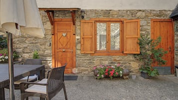 Un bâtiment en pierre avec des portes et des fenêtres en bois, une table avec des chaises et des plantes en pot.