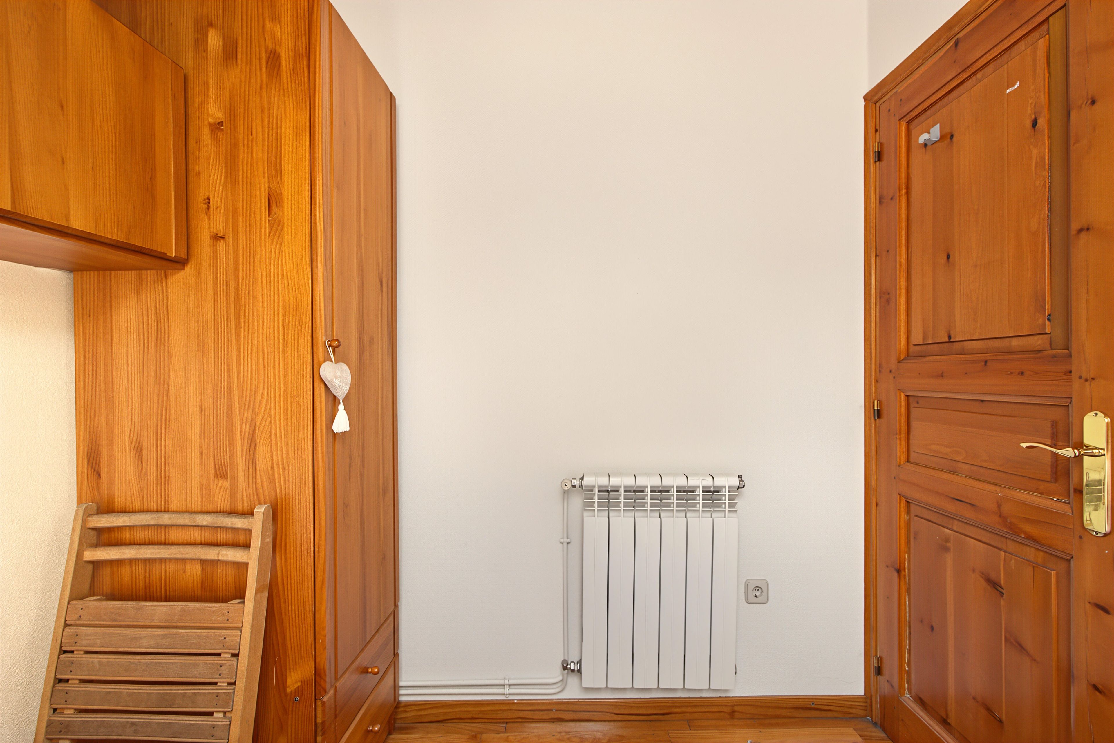 Et værelse med træskabe, en radiator og en træbænk.