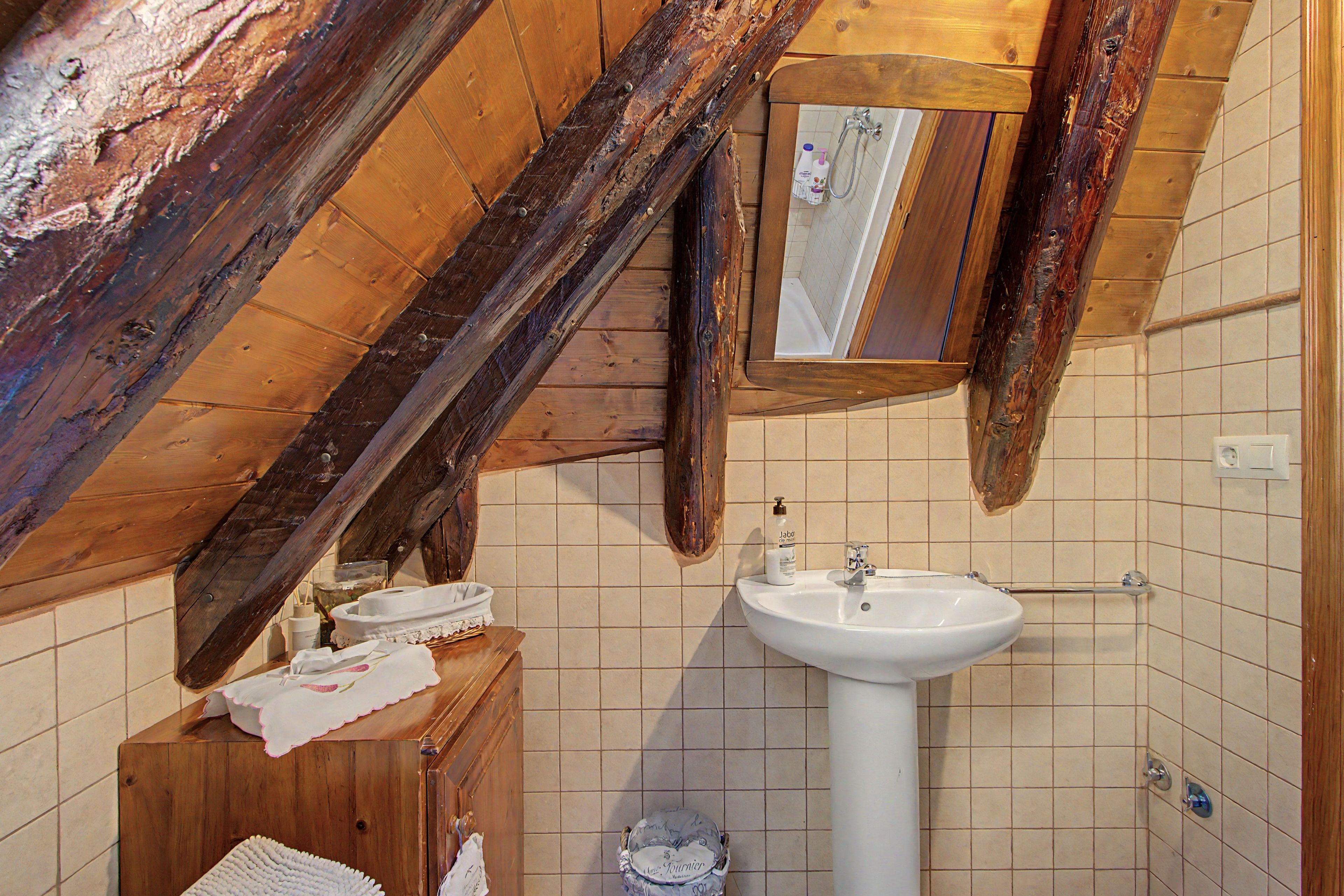 A rustic bathroom with a wooden ceiling, a white sink, and a mirror.