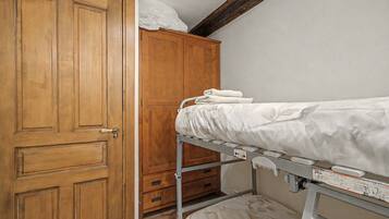 A room with a wooden wardrobe, a metal bunk bed with a mattress, and a small wooden cabinet.