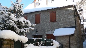 Ein Steinhaus mit schneebedecktem Dach und hölzernen Fensterläden.