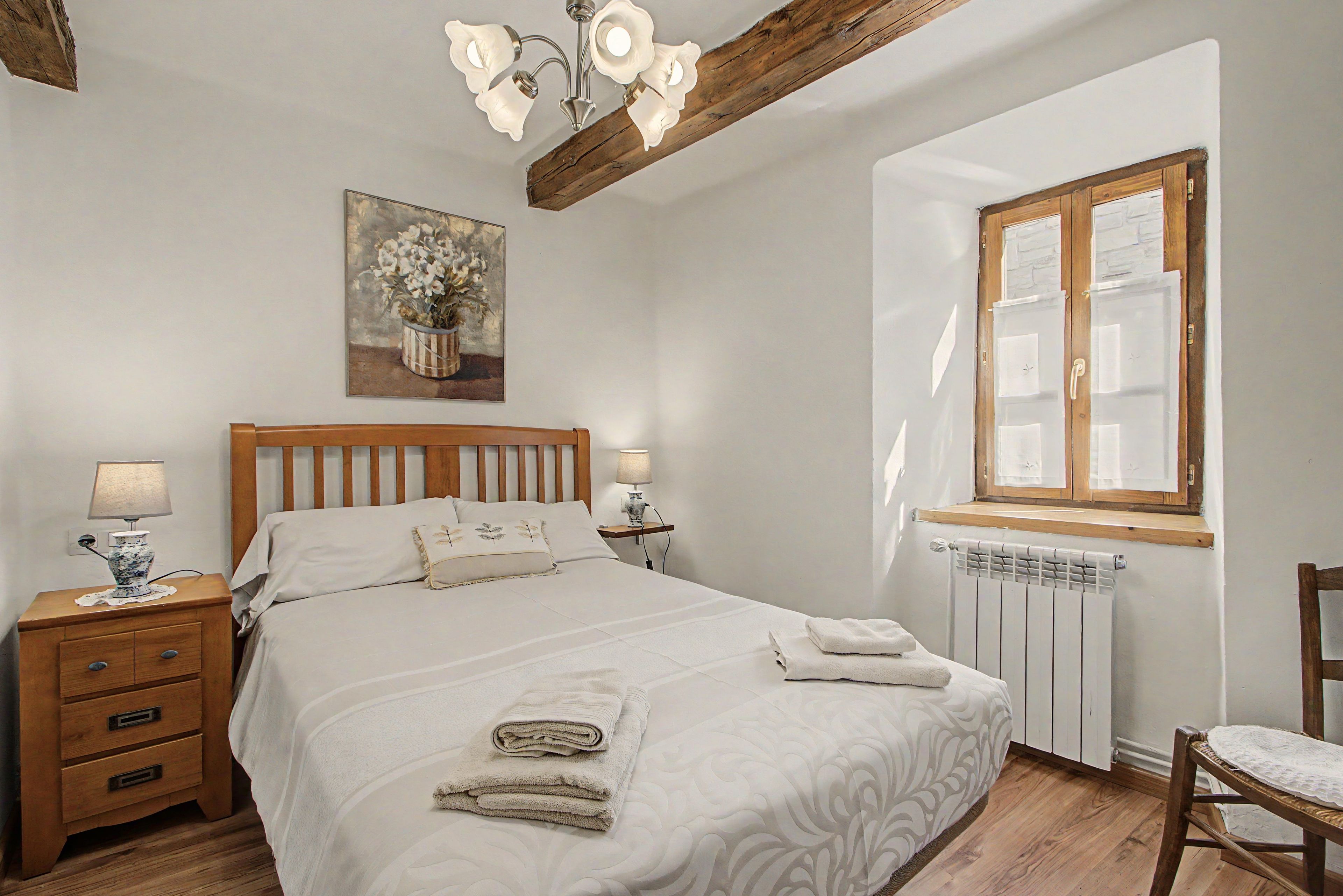 Un dormitorio con una cama de madera, lámparas de noche, un radiador y una ventana con contraventanas de madera.