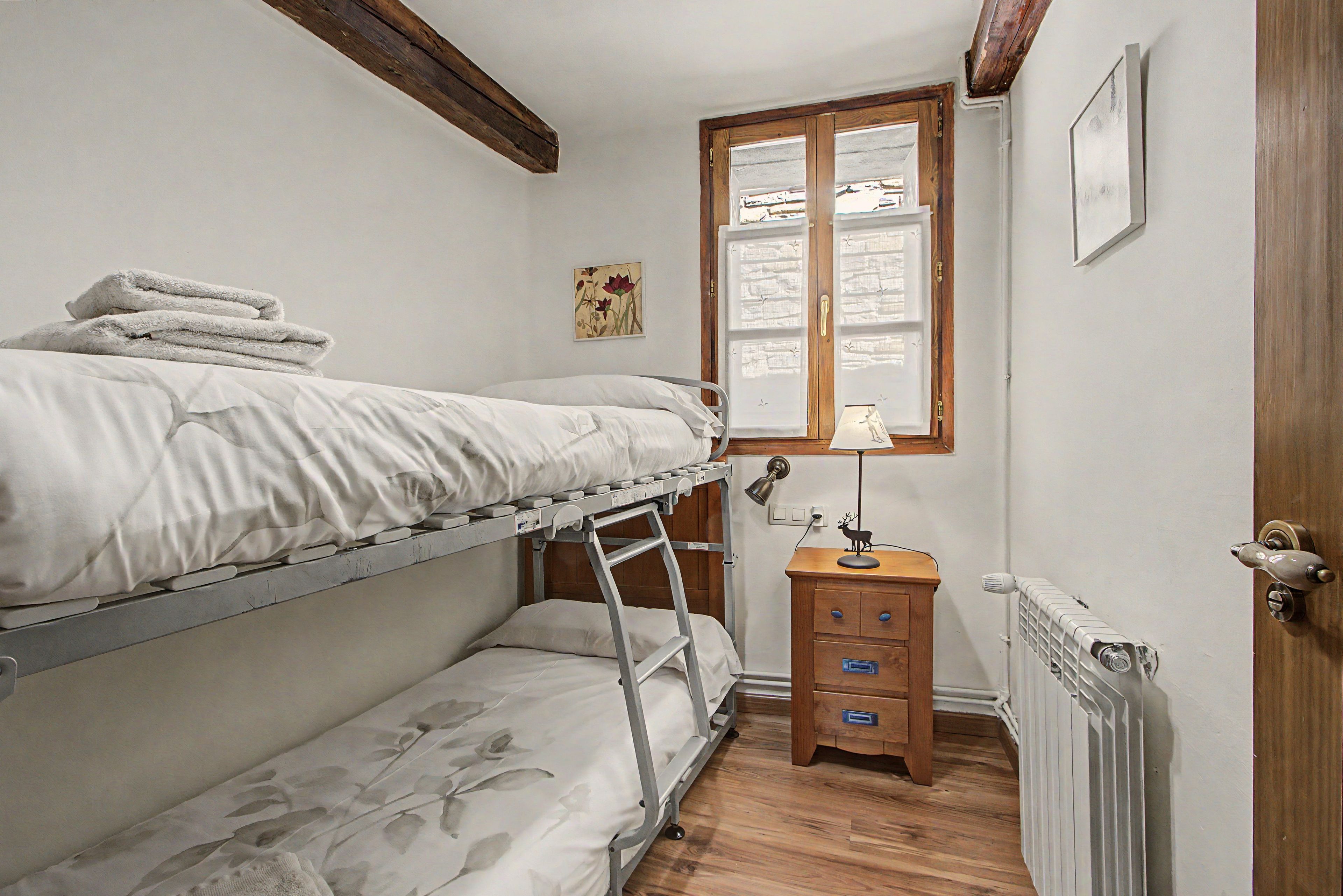 Habitación con literas, una mesita de noche de madera y un radiador.