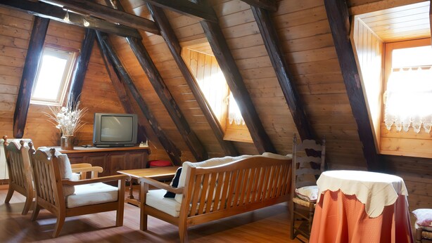 Ein Dachzimmer mit Holzbalken, einem Fernseher, einer Couch und einem Tisch.
