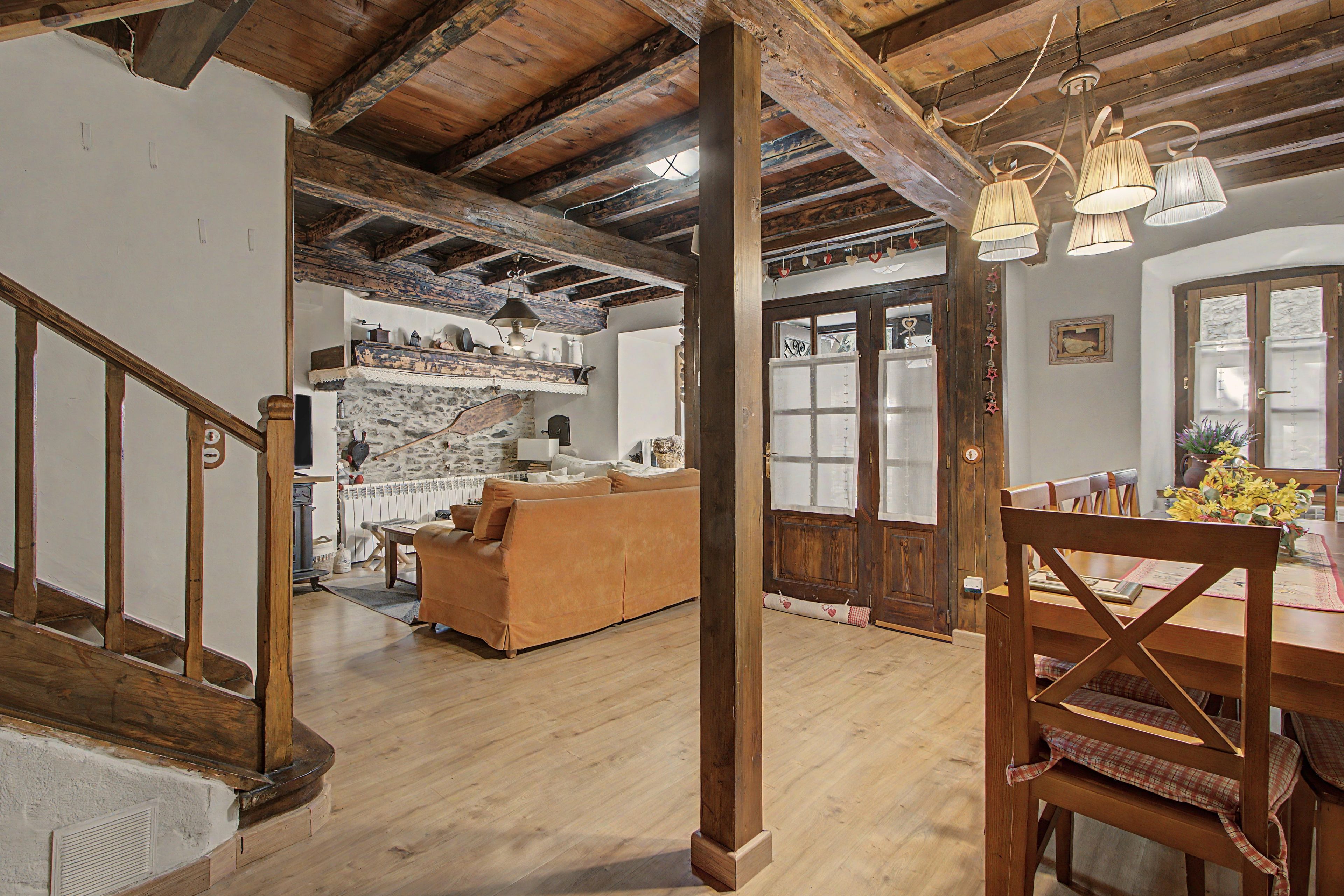 A rustic interior with exposed wooden beams, a wooden staircase, a sofa, and a dining table with chairs.