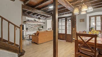 A rustic interior with exposed wooden beams, a wooden staircase, a sofa, and a dining table with chairs.