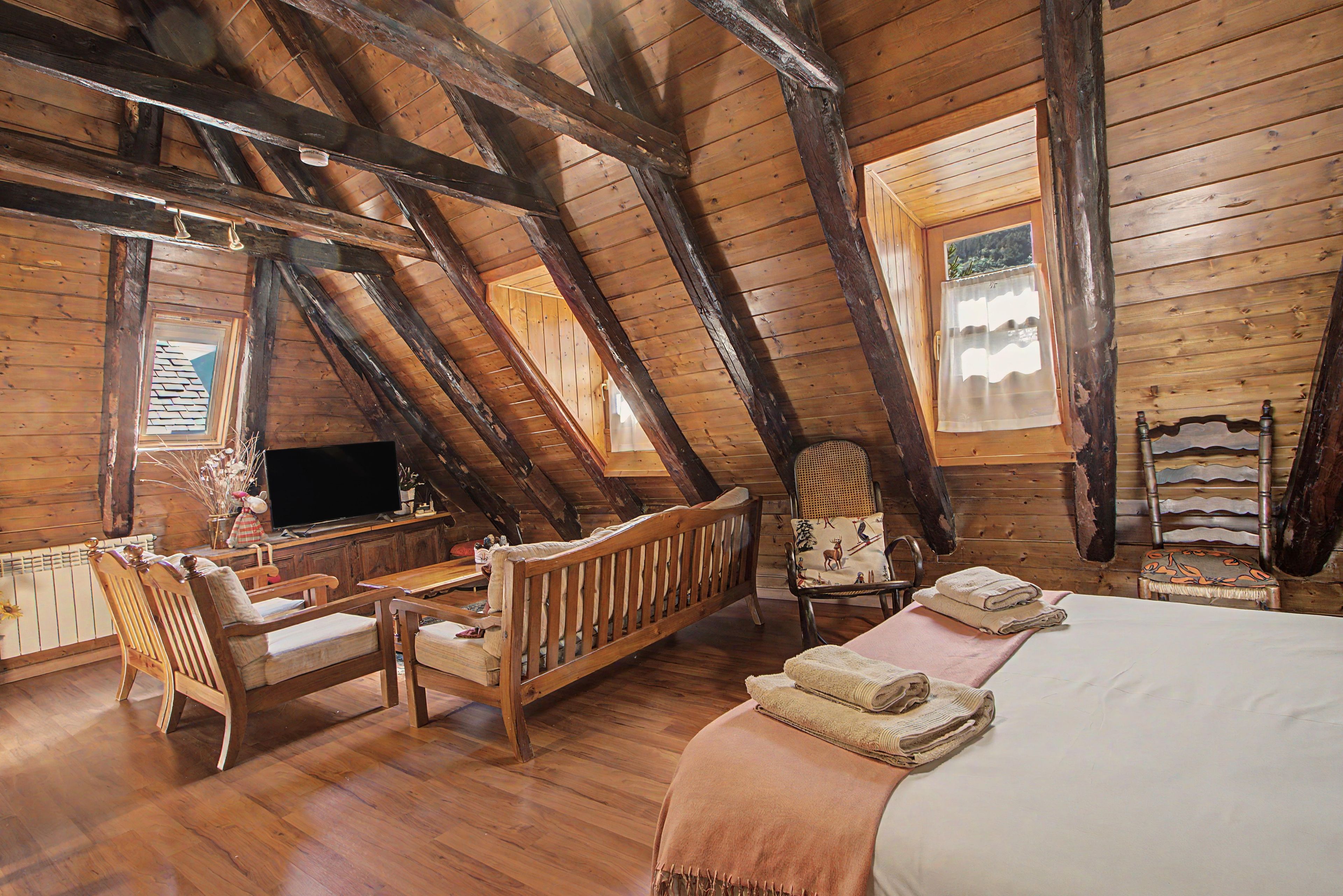 Een houten kamer met schuine wanden, een bed, een televisie en zithoeken.