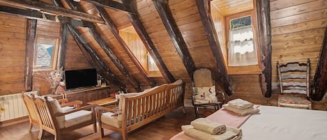 A wooden room with a sloped ceiling, a bed, a television, and seating areas.