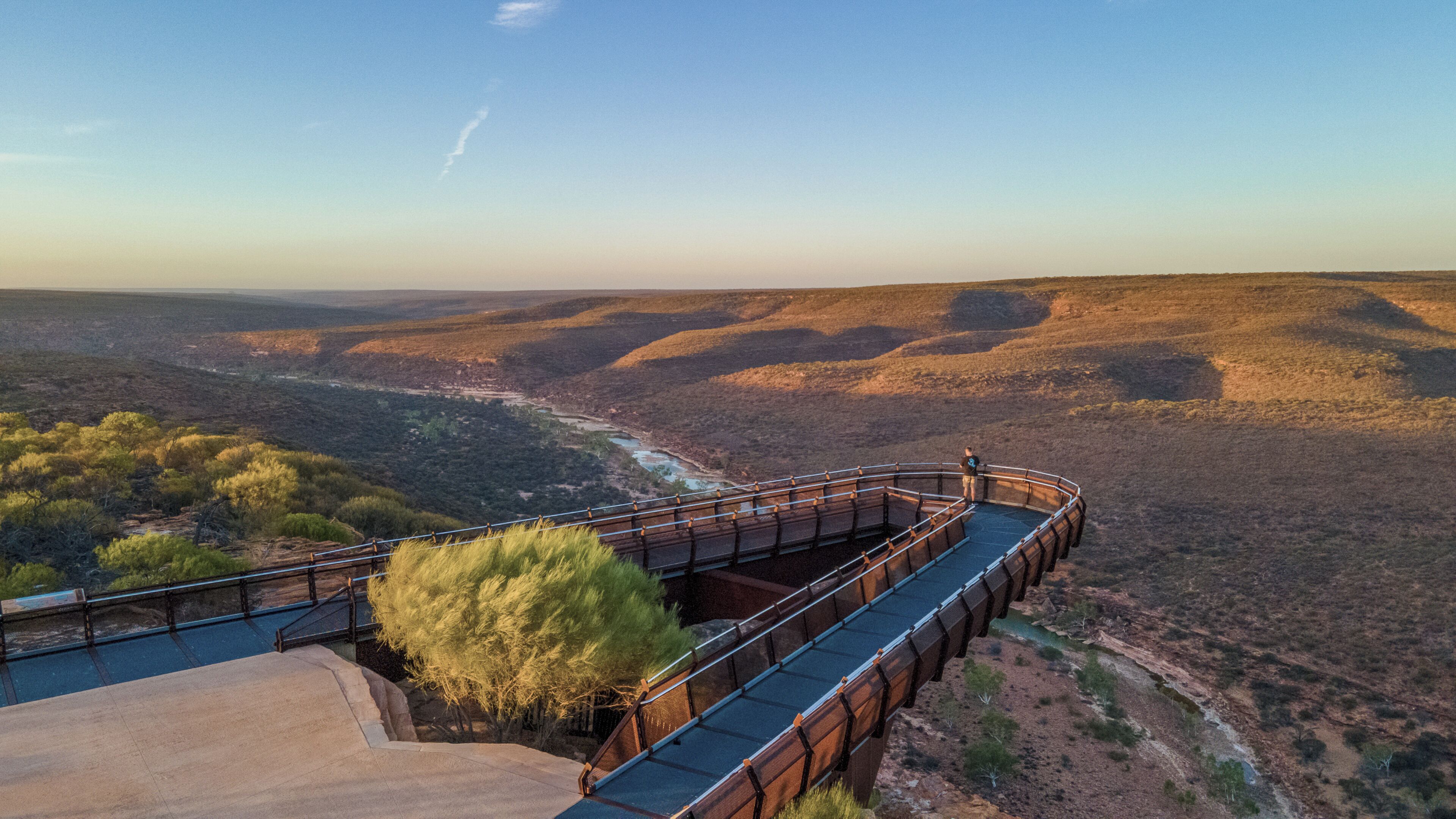 Un puente con barandilla, un río abajo y un paisaje montañoso.