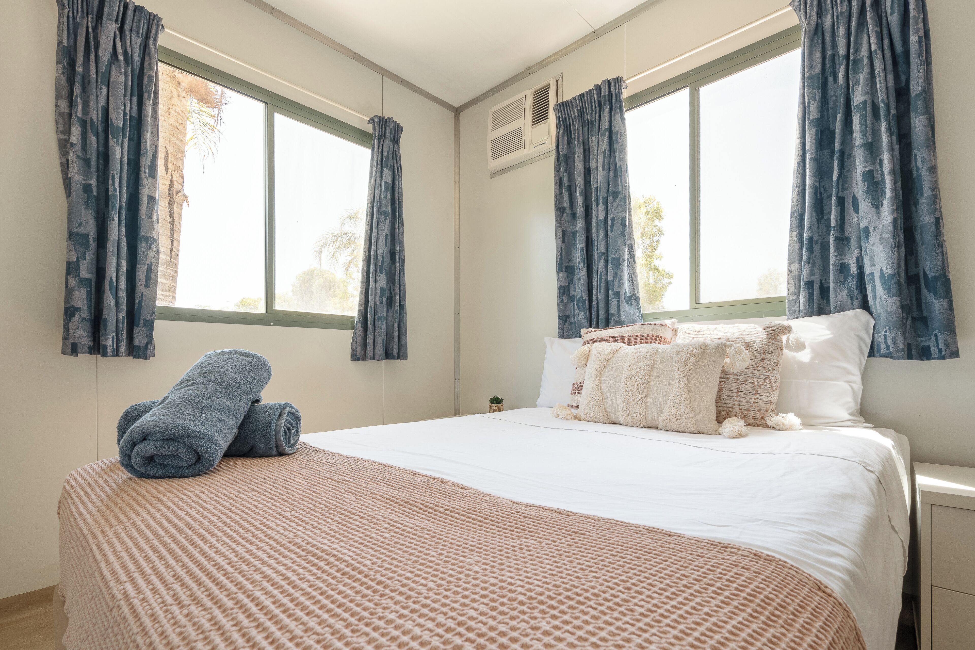 A neatly made bed with a patterned blanket, two rolled towels, and a variety of pillows.