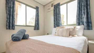 A neatly made bed with a patterned blanket, two rolled towels, and a variety of pillows.