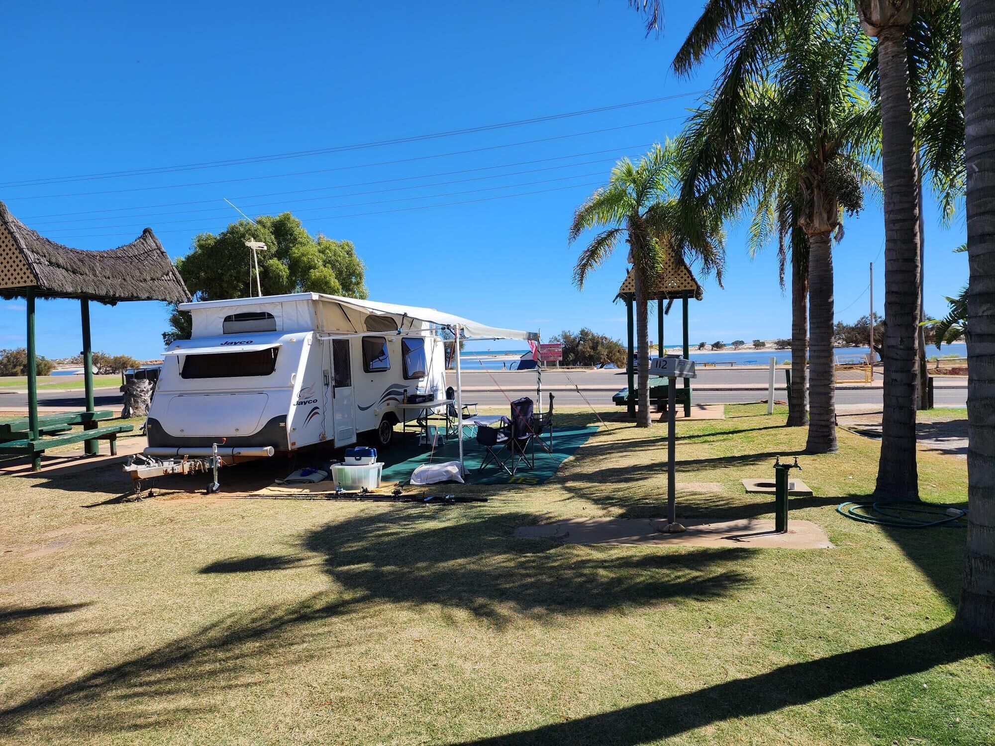 A recreational vehicle parked at a campsite with a picnic table, a small shelter, and a view of the beach.