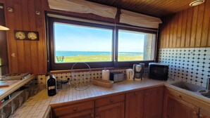 Eine Küche mit Holzausstattung, gefliestem Rücksprung, einem Fenster mit Meerblick und verschiedenen Küchengeräten.