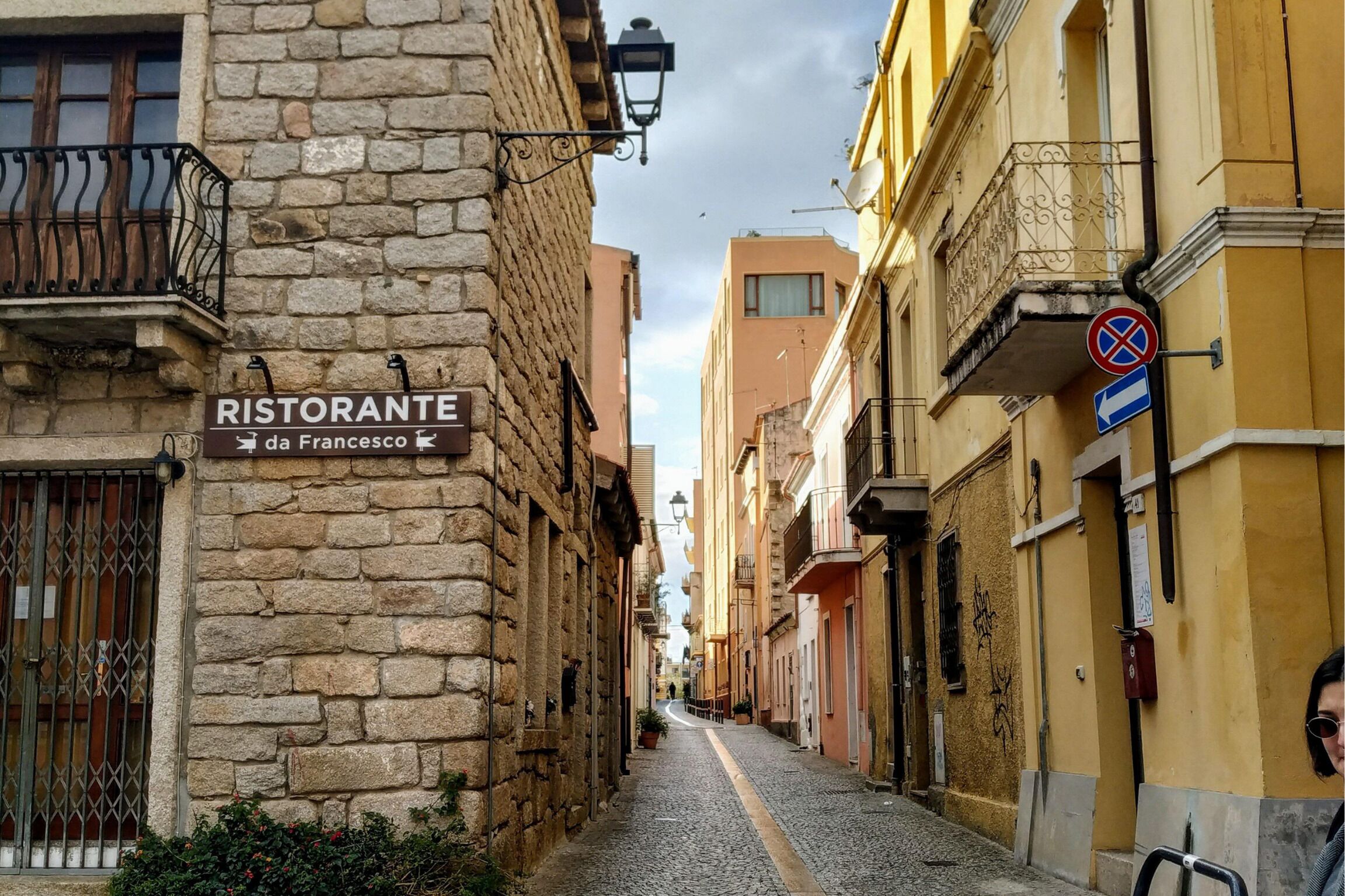A narrow cobblestone street lined with historic buildings, a sign for a restaurant named "Ristorante da Francesco," and a no parking sign.