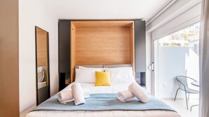 Camera d'albergo moderna con un letto grande, una testiera in legno, un cuscino giallo e vista sulla città dal balcone.