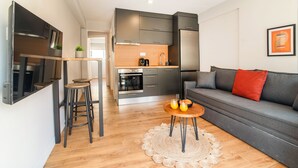 Una cucina moderna con forno a incasso e frigorifero, una zona pranzo con sgabelli e un soggiorno con divano e un cuscino rosso.