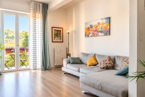 Ein Wohnzimmer mit einer Couch, einem Gemälde und Blick auf einen Balkon mit Pflanzen.