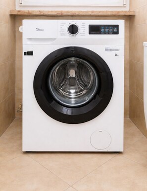 A front-loading white washing machine with a control panel, located in a tiled room.