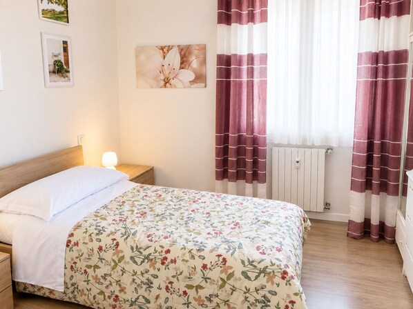 Ein Schlafzimmer mit einem Bett, einem Nachttisch, einer Wandleuchte, einem Heizkörper und Vorhängen.